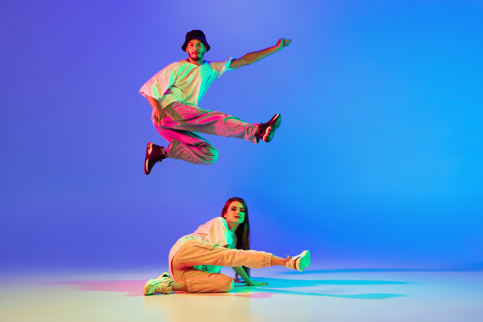 Two young people, guy and girl in casual clothes dancing contemporary dance, hip-hop over blue background in neon light.